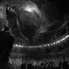 这是一幅黑暗而神秘的插图，描绘了地球上一座巨大的雕像，《失乐园-撒旦主持地狱议会》，在一个空荡荡的体育场里，灯光环绕，充满欢呼的人群，呈木炭色和白色。场景以古老古典艺术风格的详细、复杂的风格渲染，唤起一种敬畏或宏伟的感觉。在前景中，有一个极端的特写镜头，一个人聚精会神地站着，把手放在脸上，好像他在聚精会神地听他们说什么。--v 6.0 --ar 16：11 