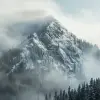 这是一座笼罩在薄雾中的山峰，周围环绕着茂密的松林，以安塞尔·亚当斯的风格拍摄。山腰被积雪覆盖，营造出一种空灵的氛围，在雾云的背景下强调了它的宏伟。使用尼康D850从下方拍摄，以获得戏剧性的视角。--ar 3：2 --v 6.0