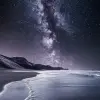 海滩上洒满星空，前方是深灰色的沙子和浅水，海平面上方可以看到银河，在夜色下形成了无尽的广阔视野。就像一个人呆在家里一样，广阔的海洋为场景增添了神秘感。黑色背景凸显细节，高对比度使一切更加生动。，真实感，--ar 59：128
