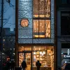 摄影、动态景观、现代主义中型商店立面设计、佳能EOS 5D Mark IV、EF 24 mm f/1.4L II USM镜头、f/2.8景深突出建筑摄影，设计应以创新和美观的方式融合不同材料，注重简洁的构图、清晰的线条和平衡的光影相互作用、日常风格、高度对比，突出立面的细节和纹理，例如材料中独特的图案或光线透过窗户的发挥，以唤起深度和现实感，重点是立面作为构图的焦点，夜晚，一些人的轮廓，汽车尾灯，
