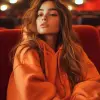 photography, vast emptiness of a movie theater serves as the backdrop for a moment of carefree repose, woman lounges across the seats, a picture of relaxed ease in an oversized orange color hoody and 