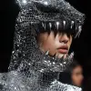 模特穿着一件由锁子甲制成的全银色服装，具有金属光泽和前卫的形状。她还有锋利的金属牙齿，看起来像鲨鱼牙线;脸上覆盖着兜帽和网状斗篷。背景颜色为深黑色，从上方点亮。这是在巴黎的一场时装秀上。时尚摄影，以前卫时尚摄影师的风格拍摄特写。--ar 85：128 --s 250